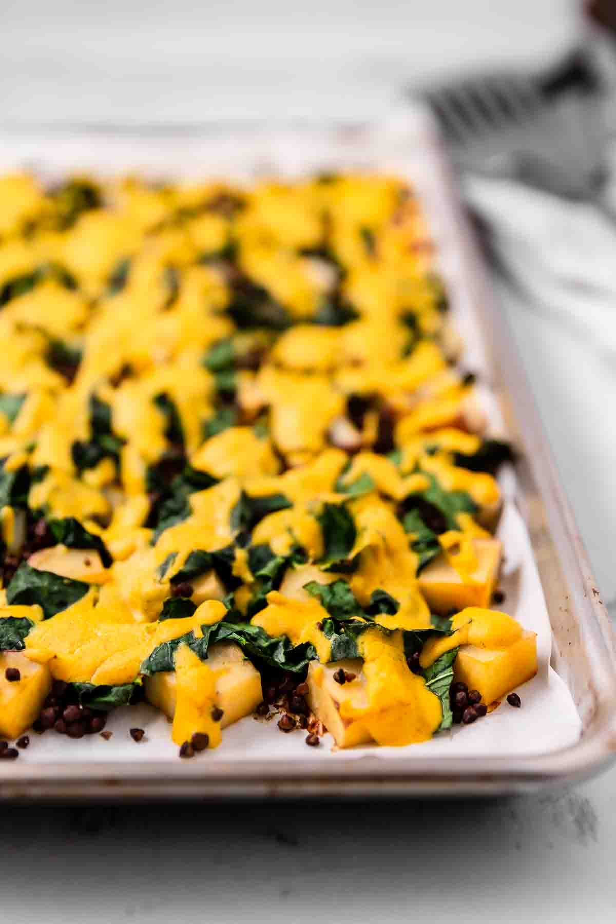 A sheet pan filled with cheesy roasted potatoes, kale, and lentils.