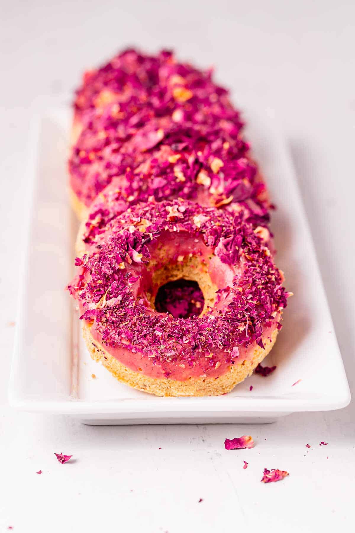 A long platter of lemon donuts topped with pink frosting and culinary rose petals.