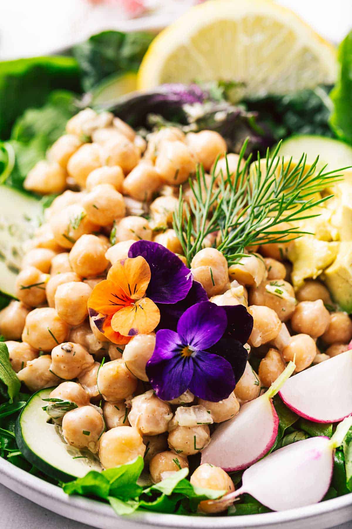 A closeup view of a vegan chickpea salad topped with purple flowers⠀⠀⠀⠀⠀⠀⠀⠀⠀