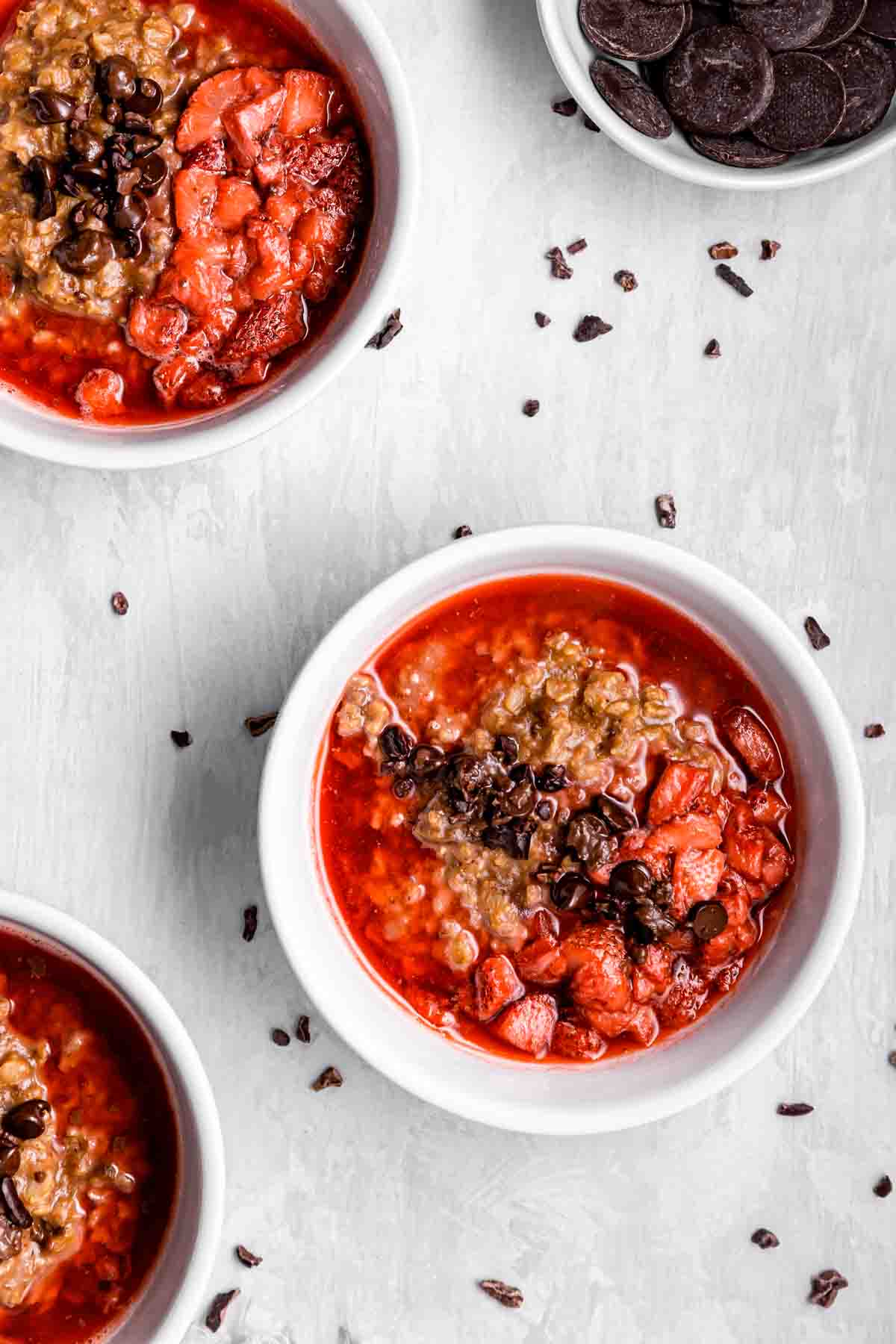 Three bowls of chocolate strawberry oatmeal on a light grey background.