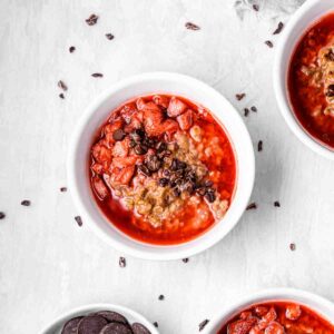 Three oatmeal bowls filled with strawberry sauce and chocolate chips and surrounded by chocolate nibs.