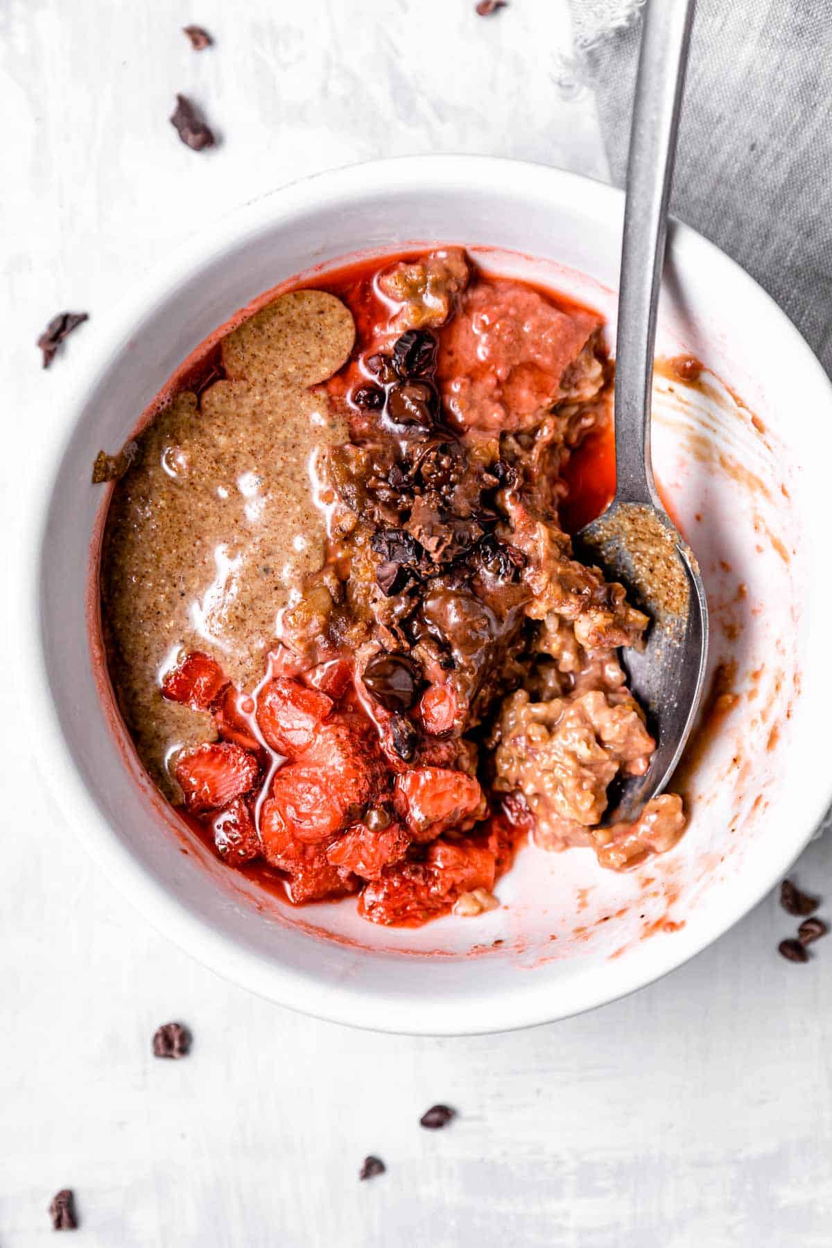 An oatmeal bowl with nut butter, strawberry sauce, and chocolate chips.