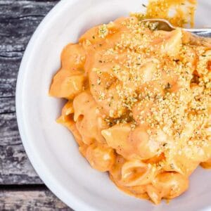 Creamy shells and cheese in a white bowl on top of a worn picnic table.