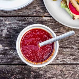 A ramekin of homemade red bbq sauce on a worn wood table.