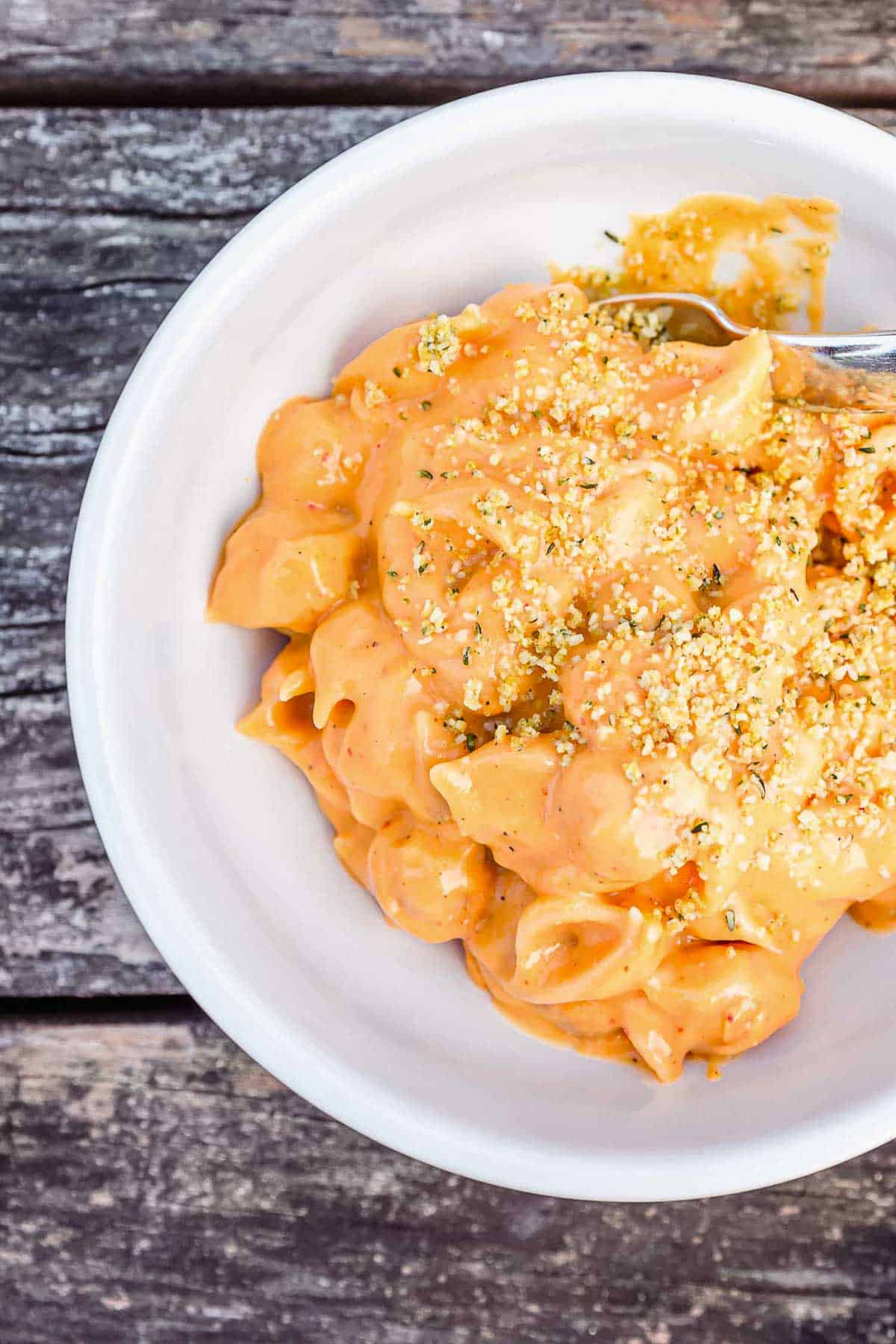 A white bowl filled with shells & cheese topped with hemp parmesan on top of a worn picnic table.