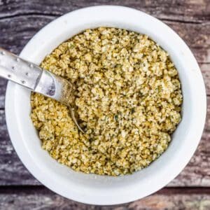 A ramekin of vegan hemp parmesan with a spoon in it, sitting on top of a weathered picnic table.