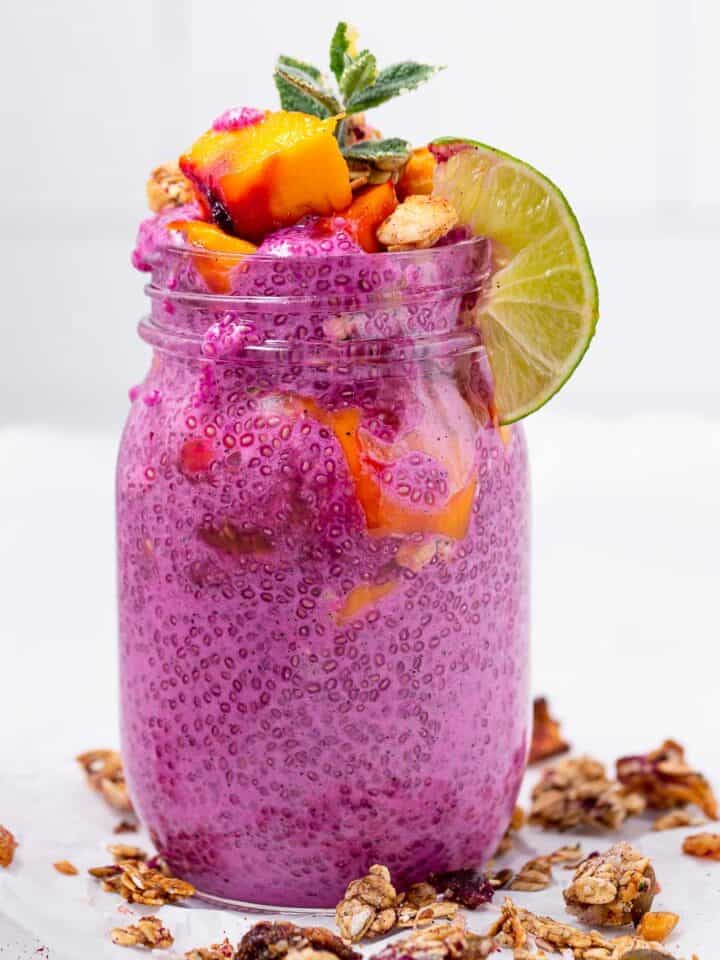 A large jar of pink chia pudding with mango, lime. mint, and tropical granola.