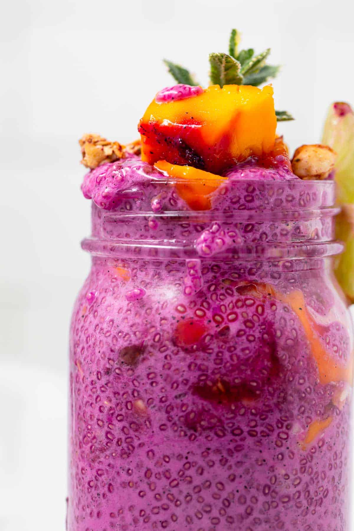 A closeup of the top of a large jar of pink dragon fruit chia pudding, topped with fresh mango and mint.