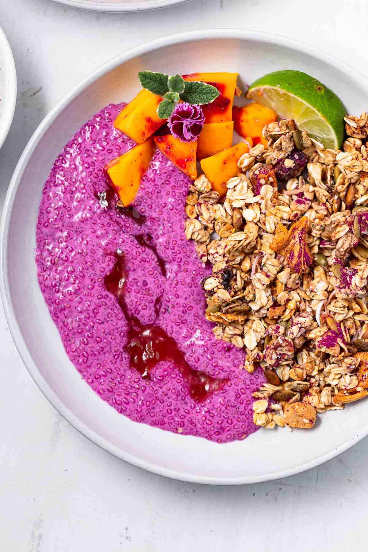 A closeup of dragon fruit chia pudding in a large bowl with mango and granola.