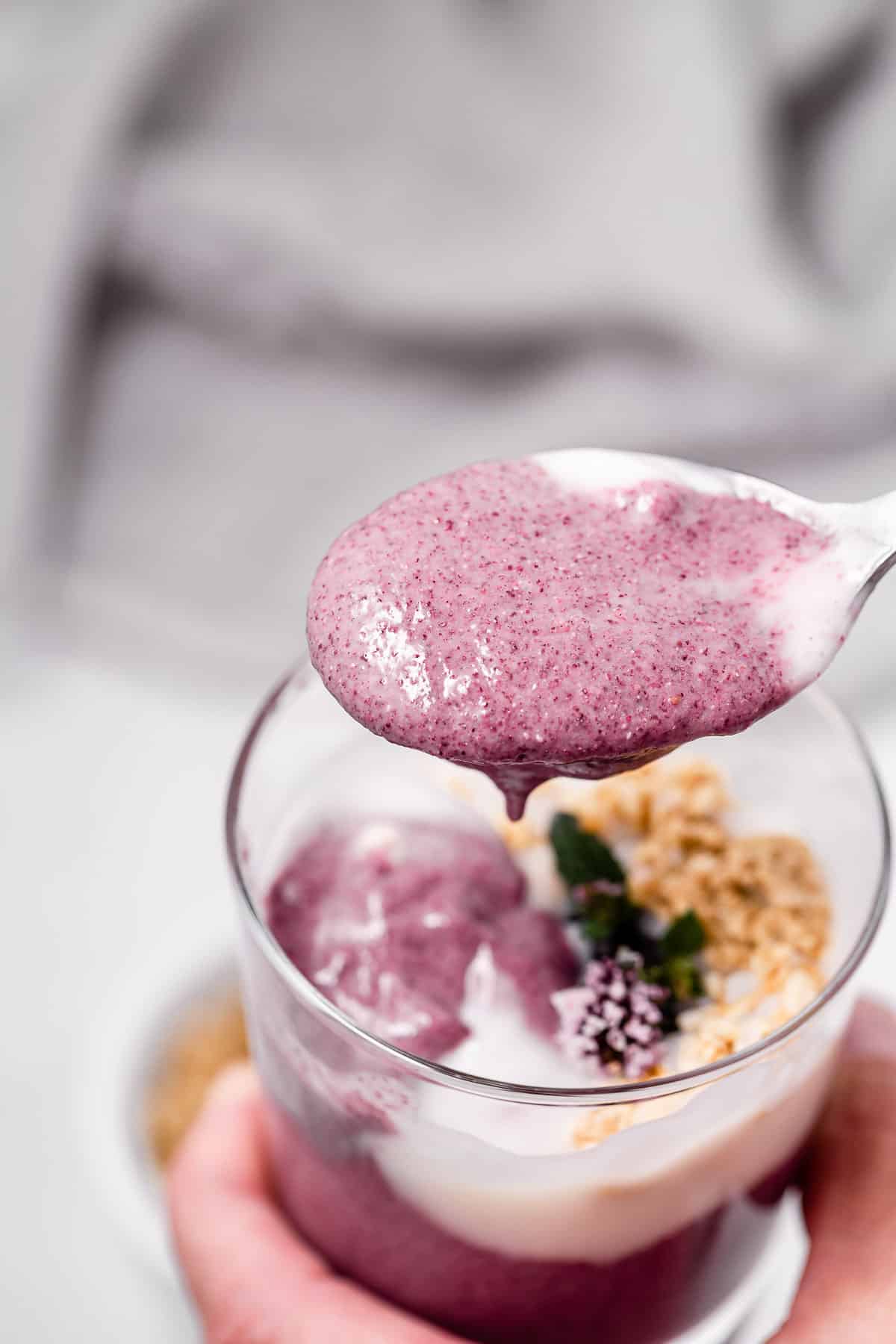 A spoonful of smooth blackberry chia pudding over a glass serving container filled with it.