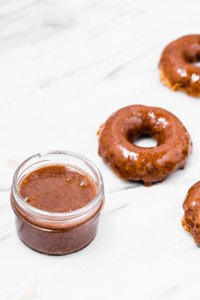 A jar of maple pecan sauce in from of frosted donuts.