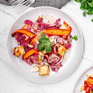 A plate of vibrant sesame tofu salad with ribbons of carrots, laying on a marble surface.