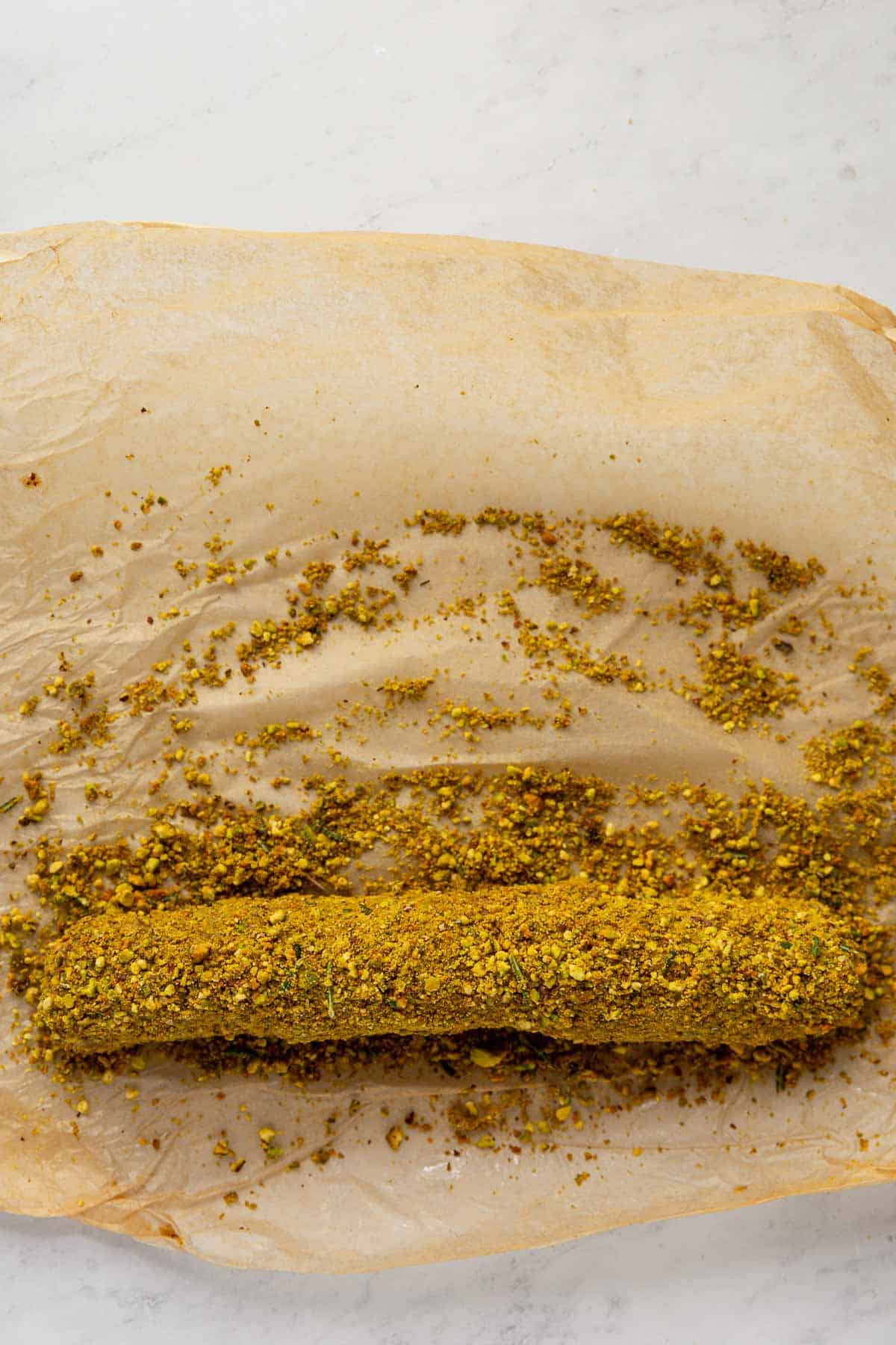 A Lemon Rosemary Vegan Cheese Log on parchment, rolled in ground pistachios.