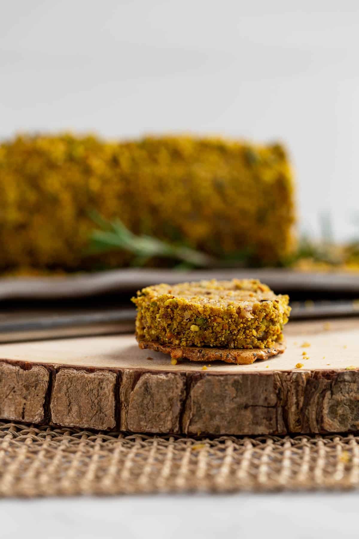 A slice of Lemon Rosemary Vegan Cheese Log on a cracker in front of the cheese log.