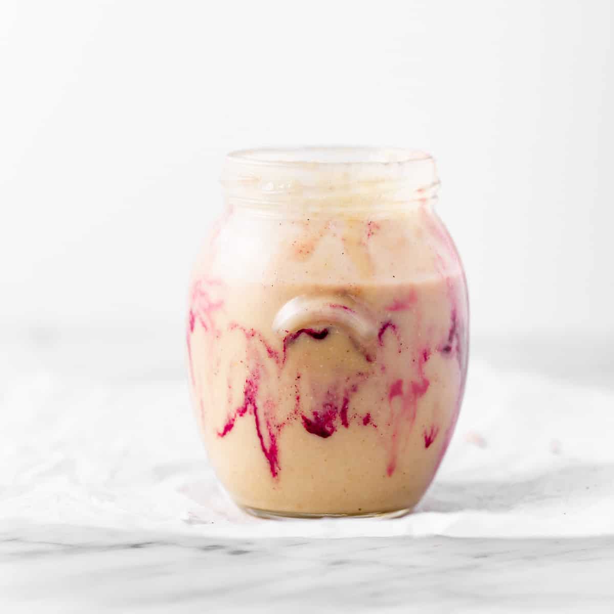 Homemade macadamia nut butter with pink swirls in a jar.