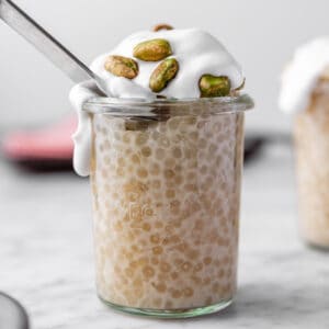 vegan vanilla tapioca pudding in a jar with spoon, topped with coconut whipped cream and pistachios