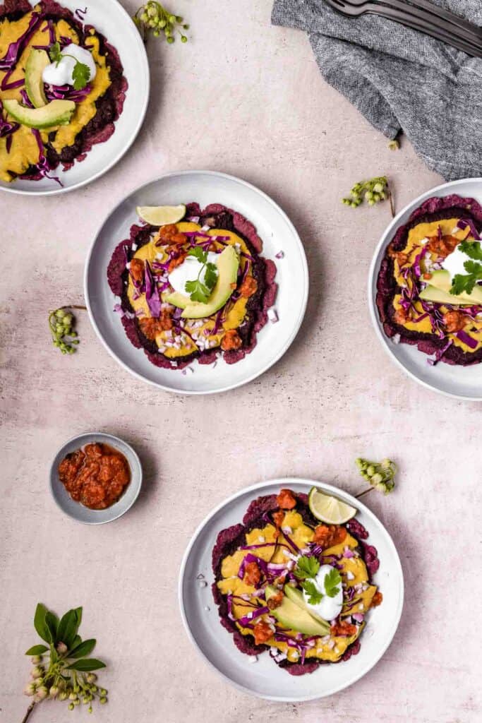 four plates each with a purple flatbread covered with vegan mexican ingredients