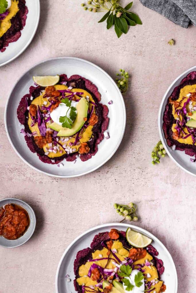 purple sweet potato flatbreads topped with vegan cheese sauce, beans, avocado, cabbage, salsa