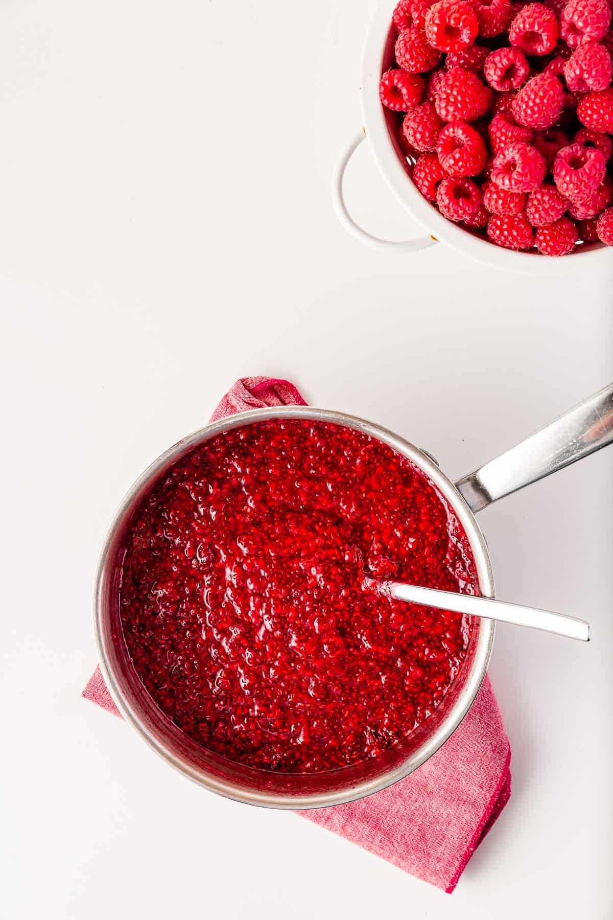 A pot filled with raspberry chia jam with a spoon inside to stir it.