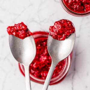 Raspberry chia jam with two spoons showing the cooked and raw versions.