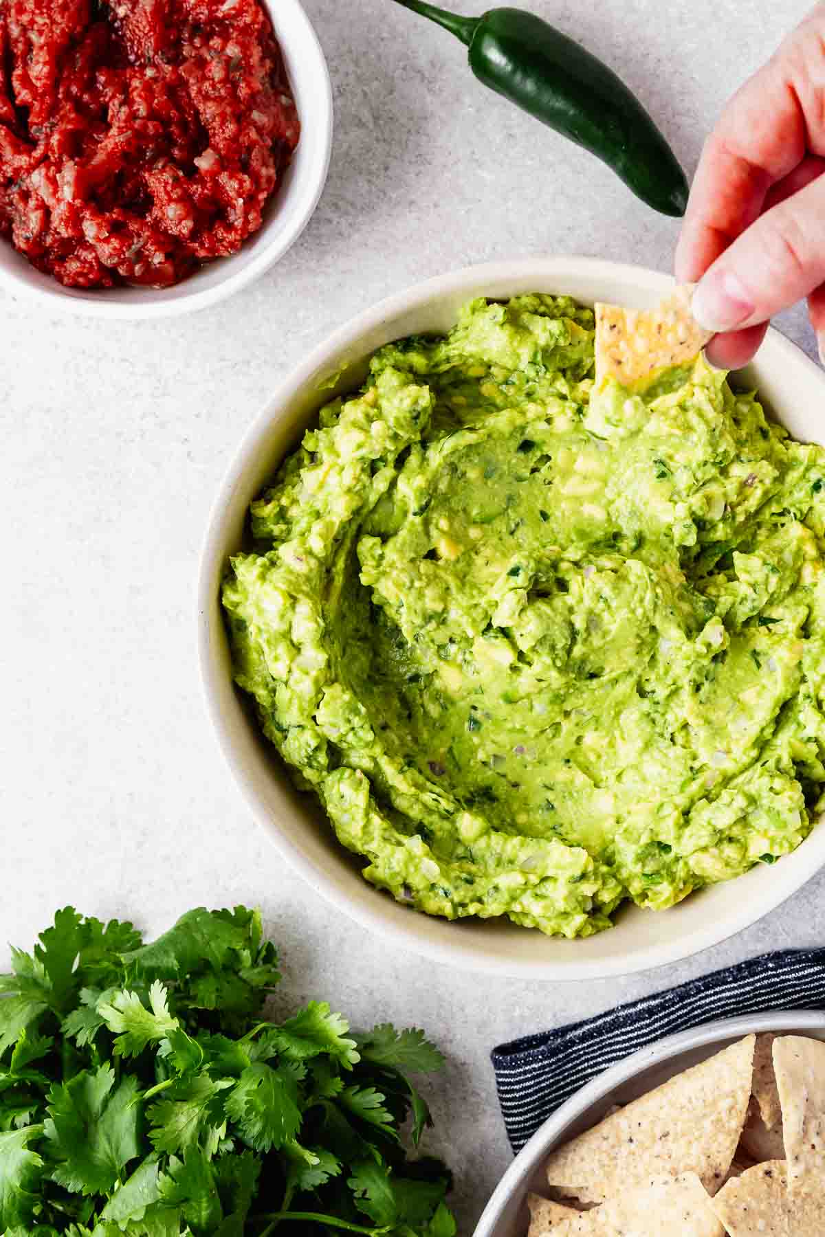 A hand dipping a tortilla chip into homemade guacamole.