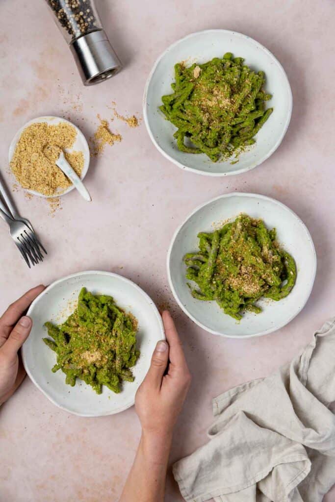 3 bowls of pesto pasta with hands reaching to one