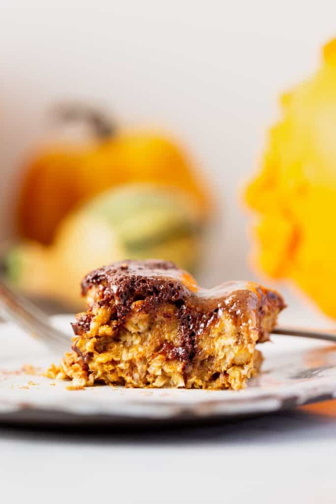 A piece of pumpkin chocolate pecan baked oatmeal on a plate surrounded by gourds