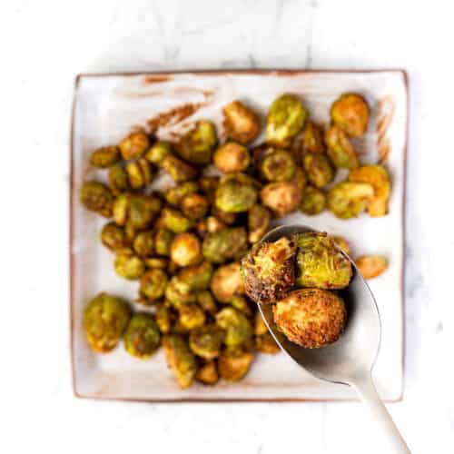 Maple balsamic roasted brussels sprouts on a square plate with a spoon holding a few.