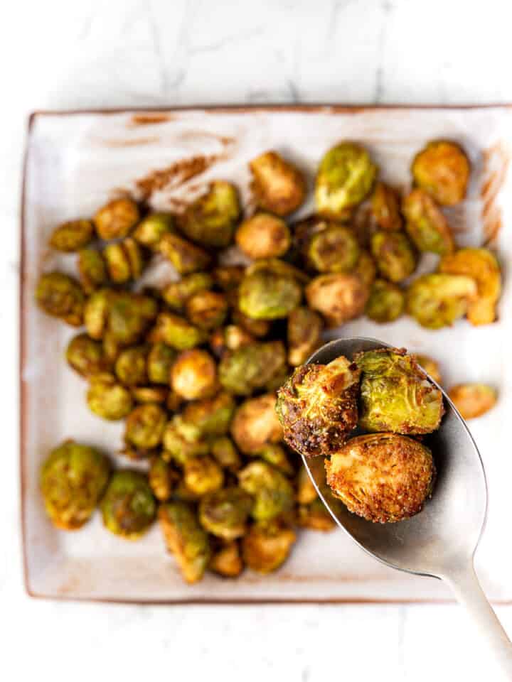 Maple balsamic roasted brussels sprouts on a square plate with a spoon holding a few.