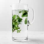 A tall pitcher filling with fresh mint water