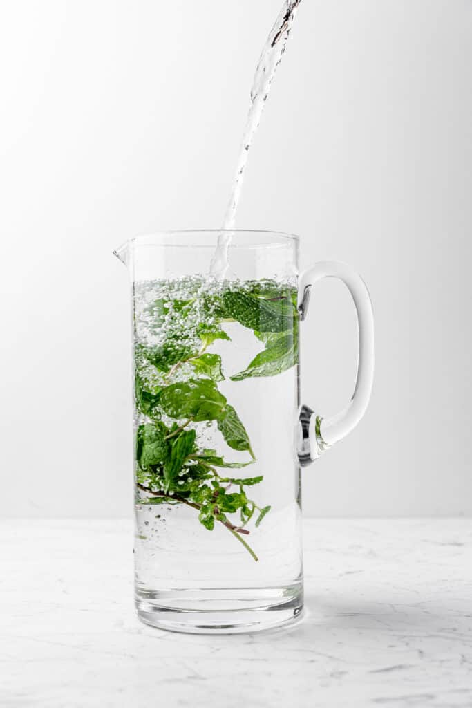 Tall pitcher filling with water and fresh mint leaves