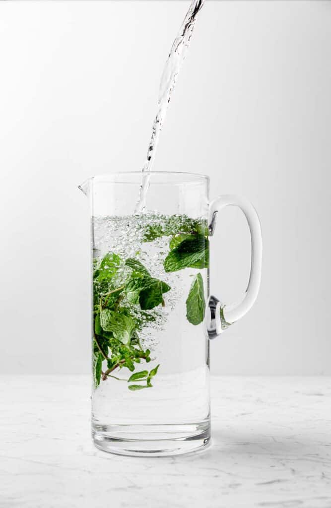 Water filling a pitcher with fresh mint sprigs