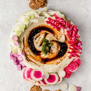 Smooth, creamy hummus topped with balsamic glaze and surrounded by bright, colorful veggies and flax crackers