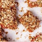 Strawberry rhubarb bars on white parchment paper with crumbs.