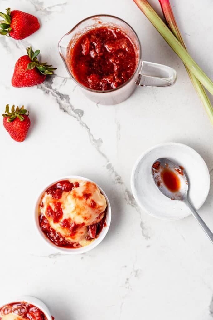 a pitcher of strawberry rhubarb compote with a cup of orange sorbet topped with compote