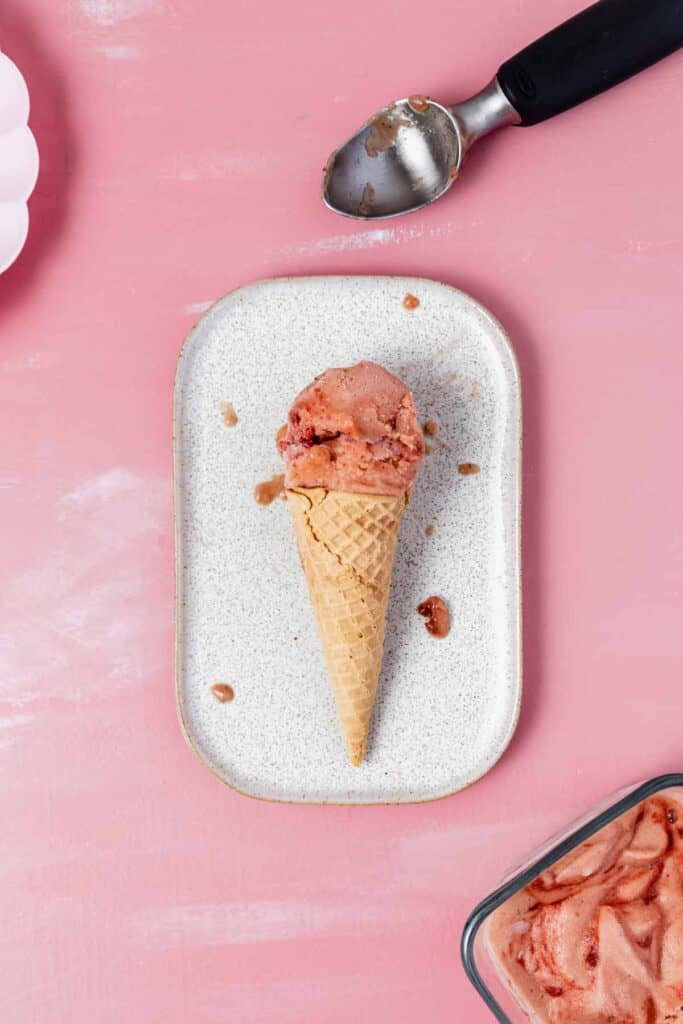 a scoop of strawberry rhubarb nice cream in a cone on a rectangular plate