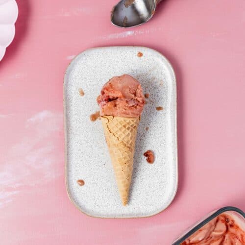 a scoop of strawberry rhubarb nice cream in a cone on a rectangular plate