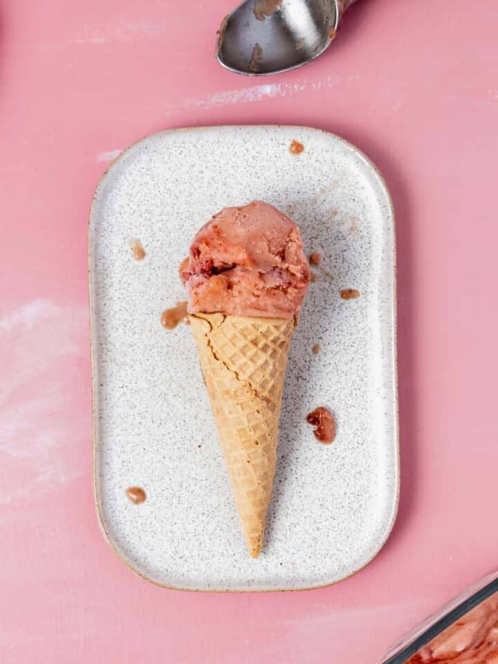 a scoop of strawberry rhubarb nice cream in a cone on a rectangular plate