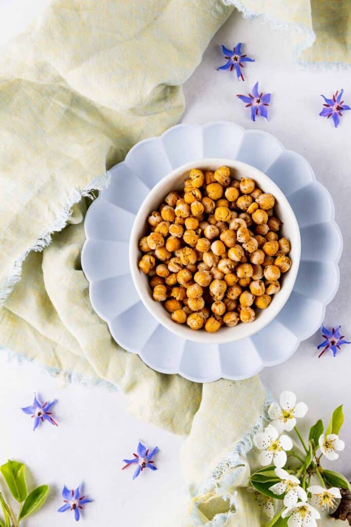 Crispy chickpeas in a bowl surrounded by periwinkle flowers and a green linen