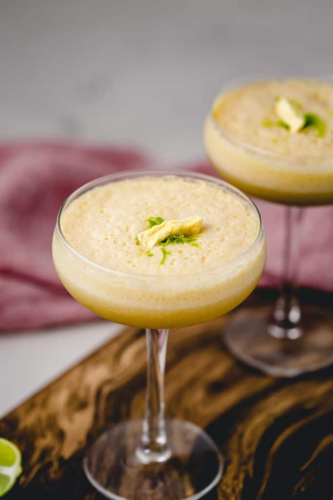 A closeup view of a Piña Colada topped with lime zest and freeze dried pineapple slice.