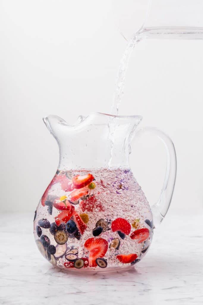 A red, white, and blue drink that is simply fruit, herbs, and water in a large pitcher