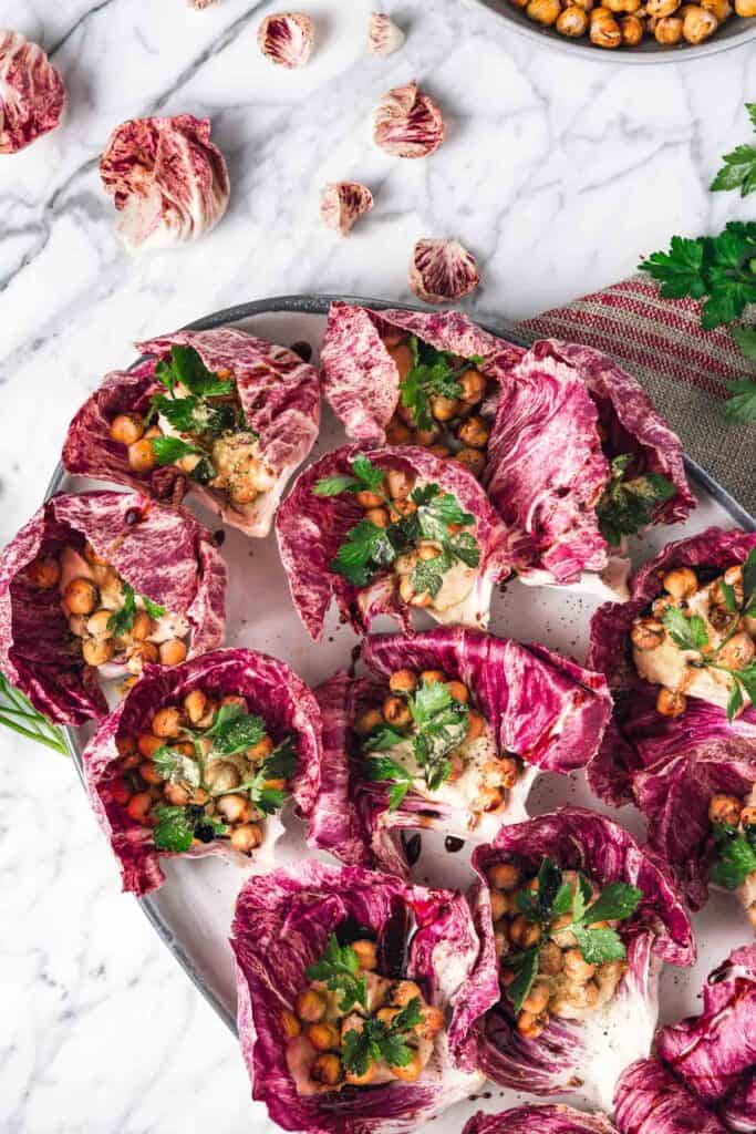 Closeup view of a platter of radicchio leaves stuffed with hummus and crispy chickpeas.