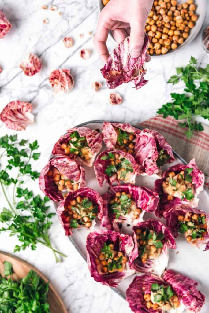 a hand reaching for a hummus stuffed radicchio appetizer