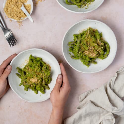 hands reaching for one of three pesto pasta bowls