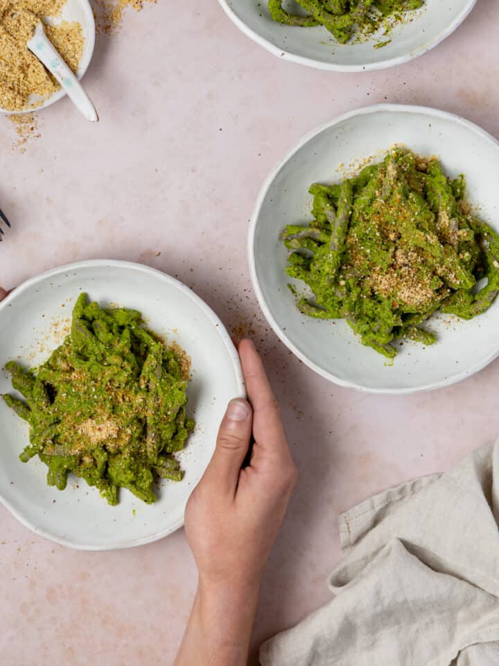 hands reaching for one of three pesto pasta bowls