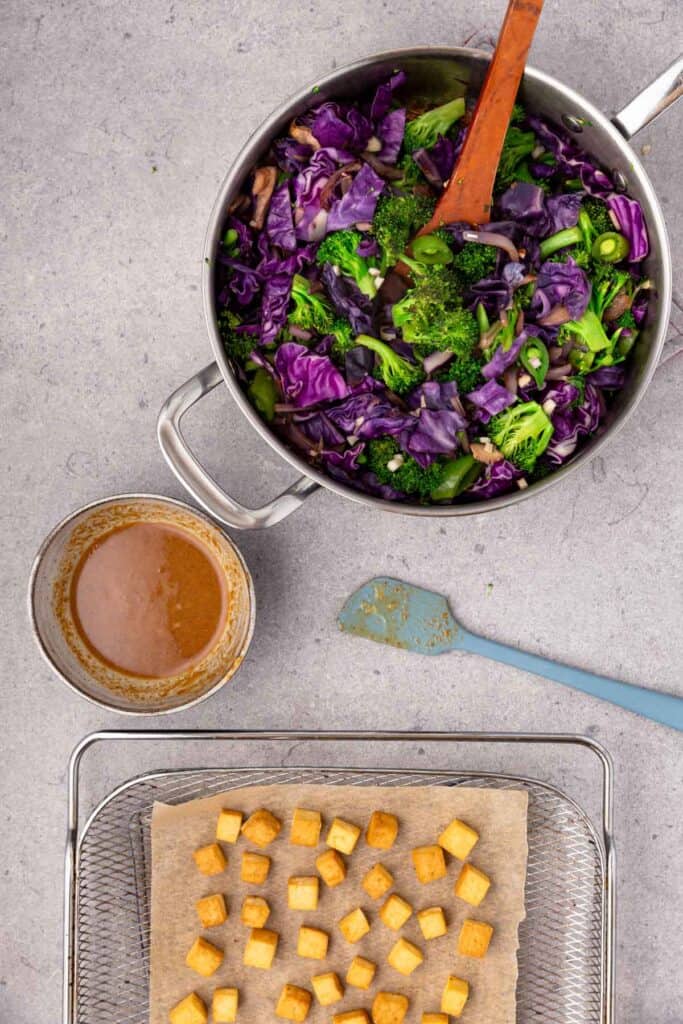 Tofu on an air fryer rack, a bowl of sauce, and a pot of veggies