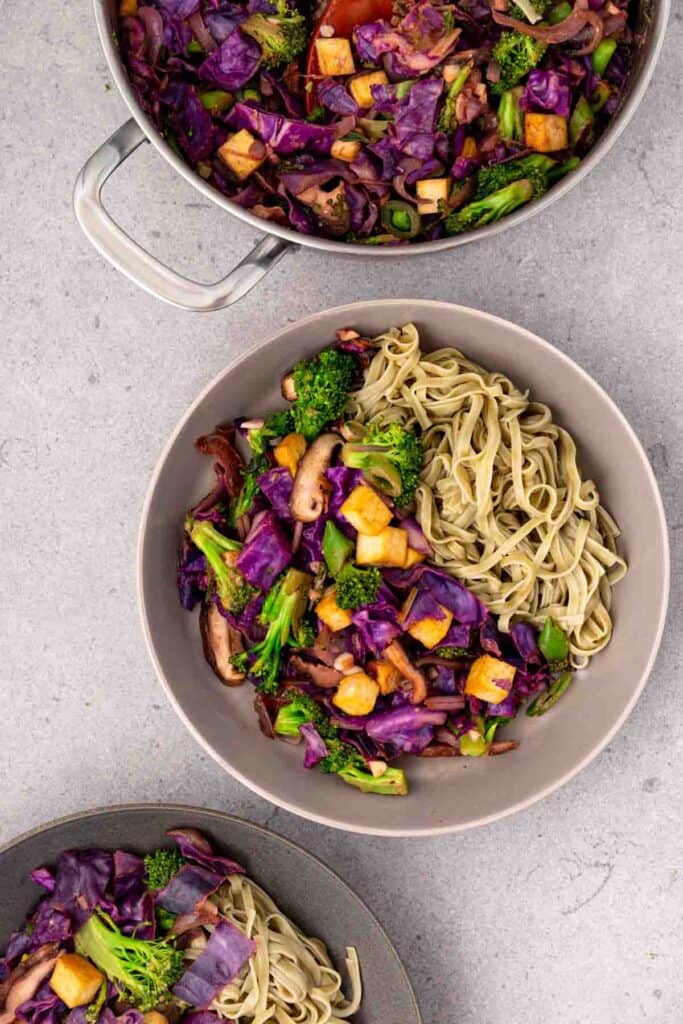 Two bowls of purple and green tofu stir fry with the pot of stir fry