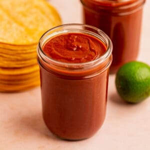 a jar of homemade enchilada sauce with corn tortillas and a lime