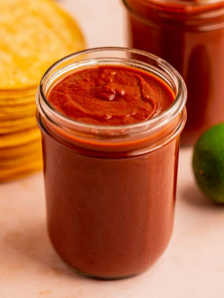 a jar of homemade enchilada sauce with corn tortillas and a lime