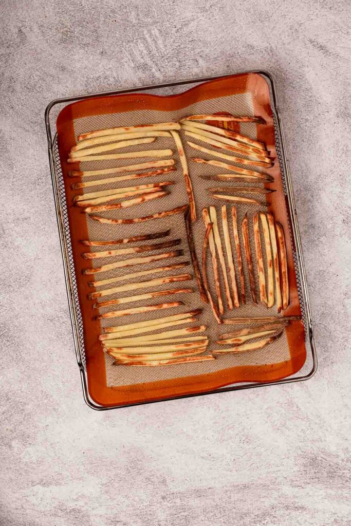 An air fryer tray lined with a silpat and baked french fries.